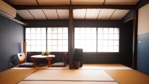 A tatami mat room with a low table, two cushions, a chair, and a window with a view.