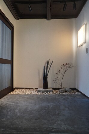 A minimalist interior with a concrete floor, a small rock garden, and a decorative branch in a vase. - Yuurakuan (Kyoto)
