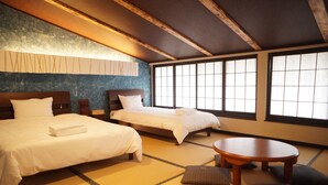 A traditional Japanese-style room with tatami flooring, two beds, a round wooden table, and a large window providing natural light.