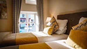 A hotel room with two beds, a window with curtains, and a view of a building outside. - Kingstons Townhouse (Killorglin)