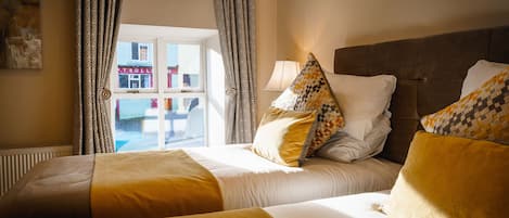 Habitación de hotel con dos camas, una ventana con cortinas y vista a un edificio.