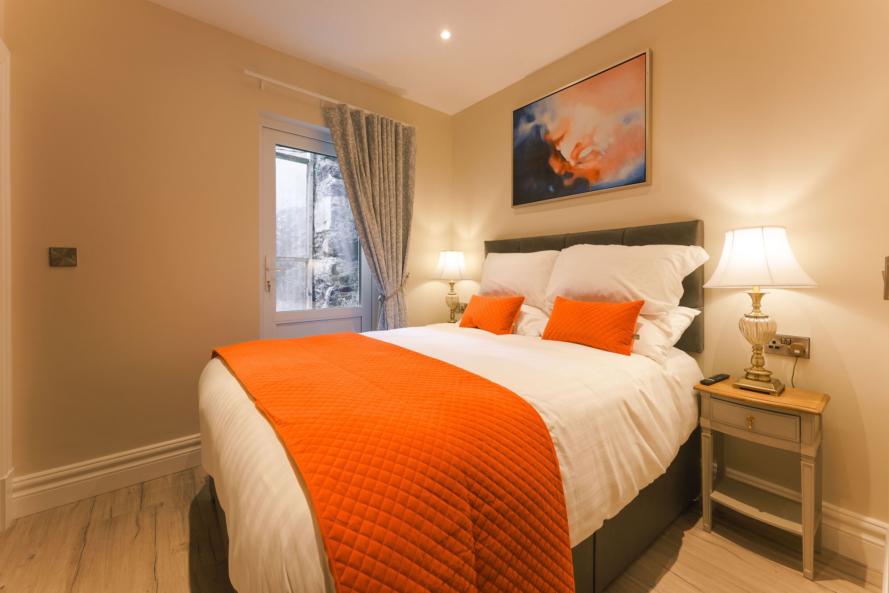 A bedroom with a large bed, two bedside lamps, a nightstand, and a window with curtains.