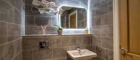 A modern bathroom with dark tiles, a white sink, a mirror, and a wooden door.