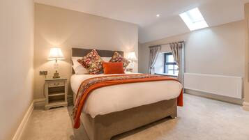 A bedroom with a large bed, two bedside tables with lamps, a window with curtains, and a skylight.