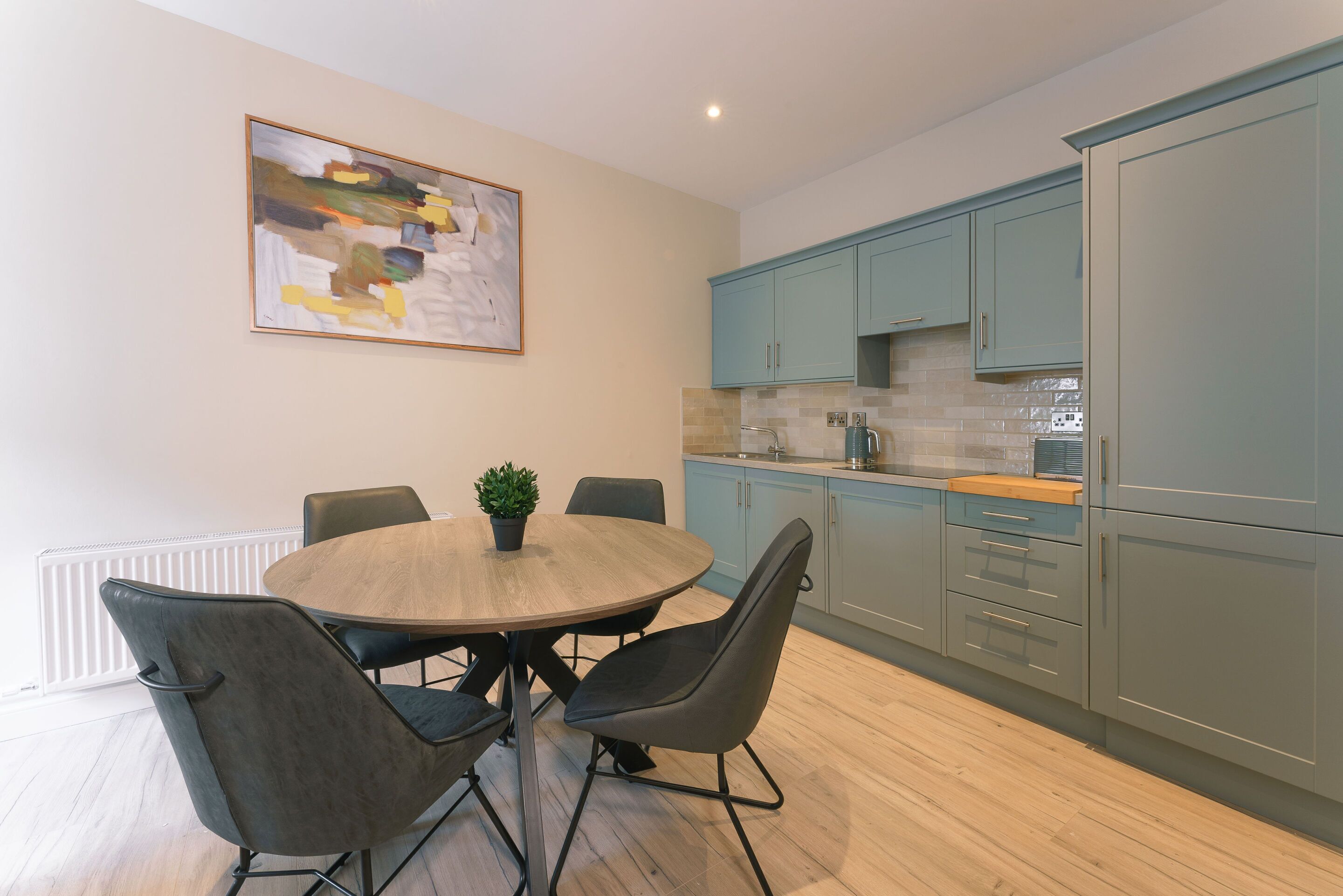 Una cocina moderna con armarios azul claro, una mesa redonda de madera con sillas y una planta en maceta.