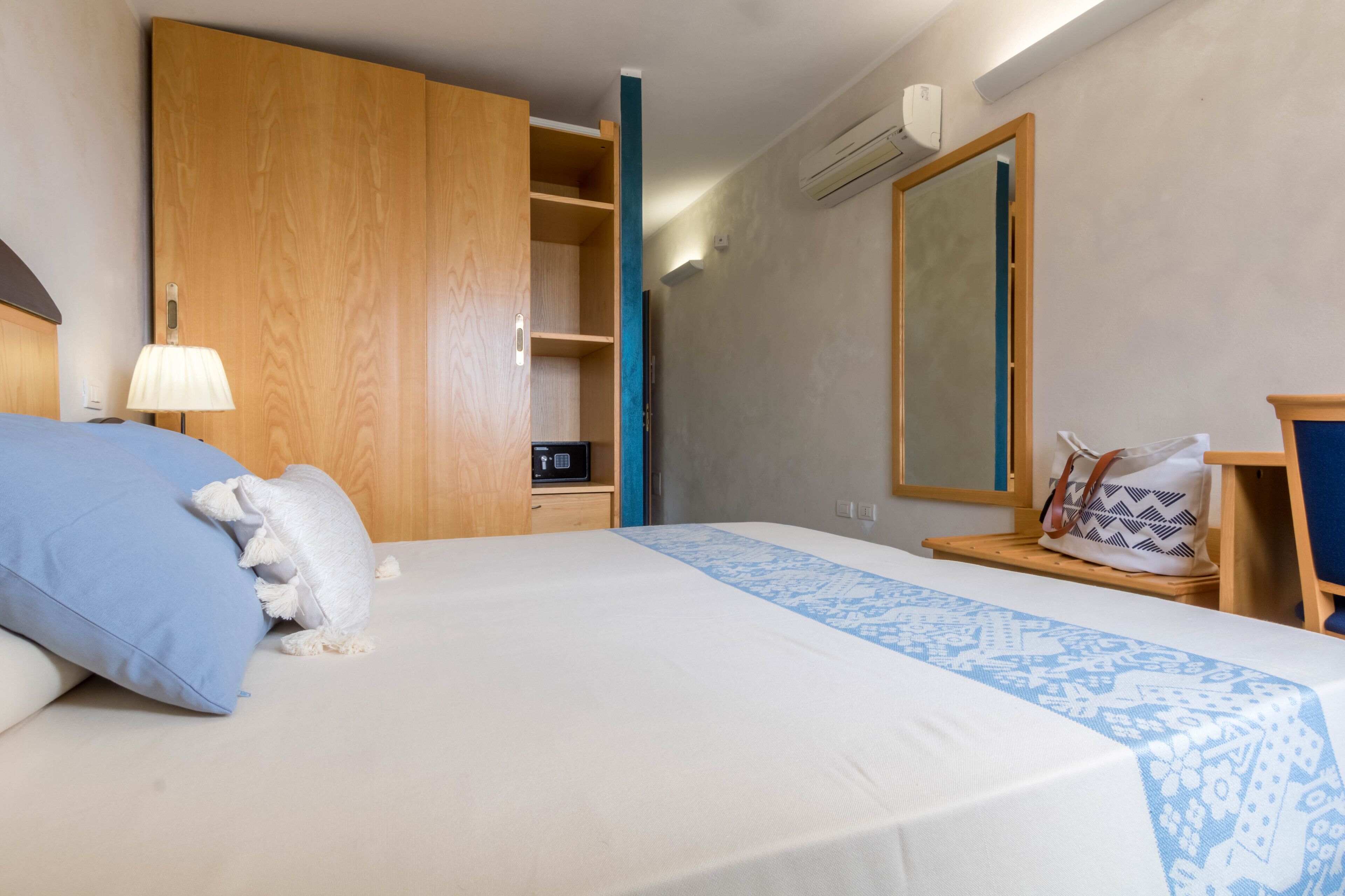 Une chambre à coucher avec un lit, une armoire en bois, un miroir, une table de chevet et une lampe.