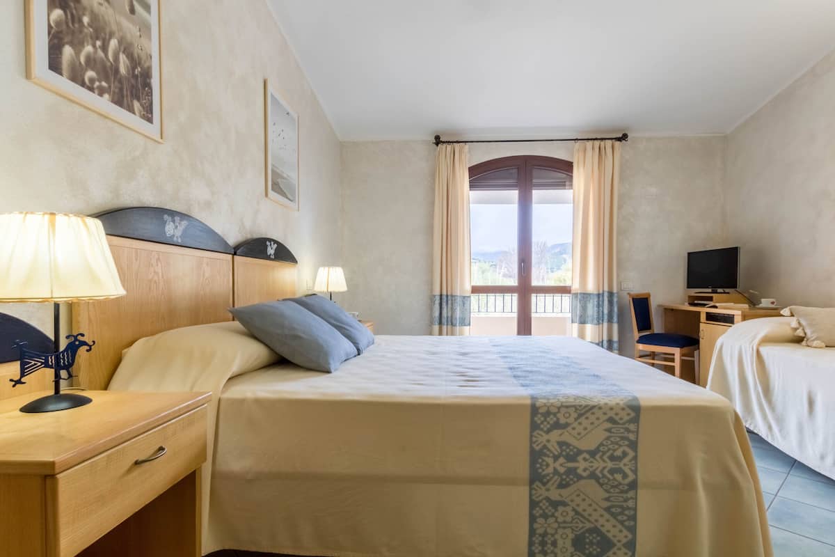 A hotel room with a bed, a desk with a computer, a TV, and a window with curtains.