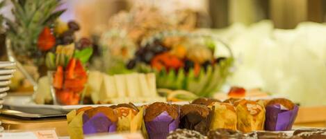 Un bufé con muffins, un bol de fruta y un letrero que indica 'Muffins' y 'Scones'.