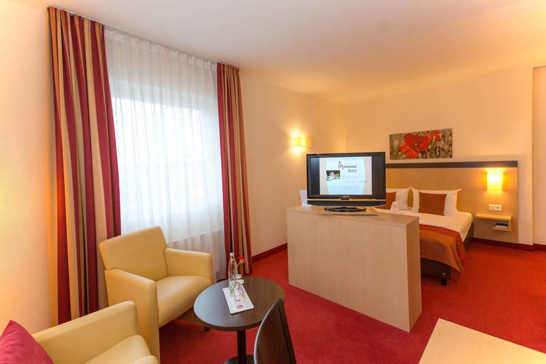 A hotel room with a bed, a TV, a desk, a chair, and a table.