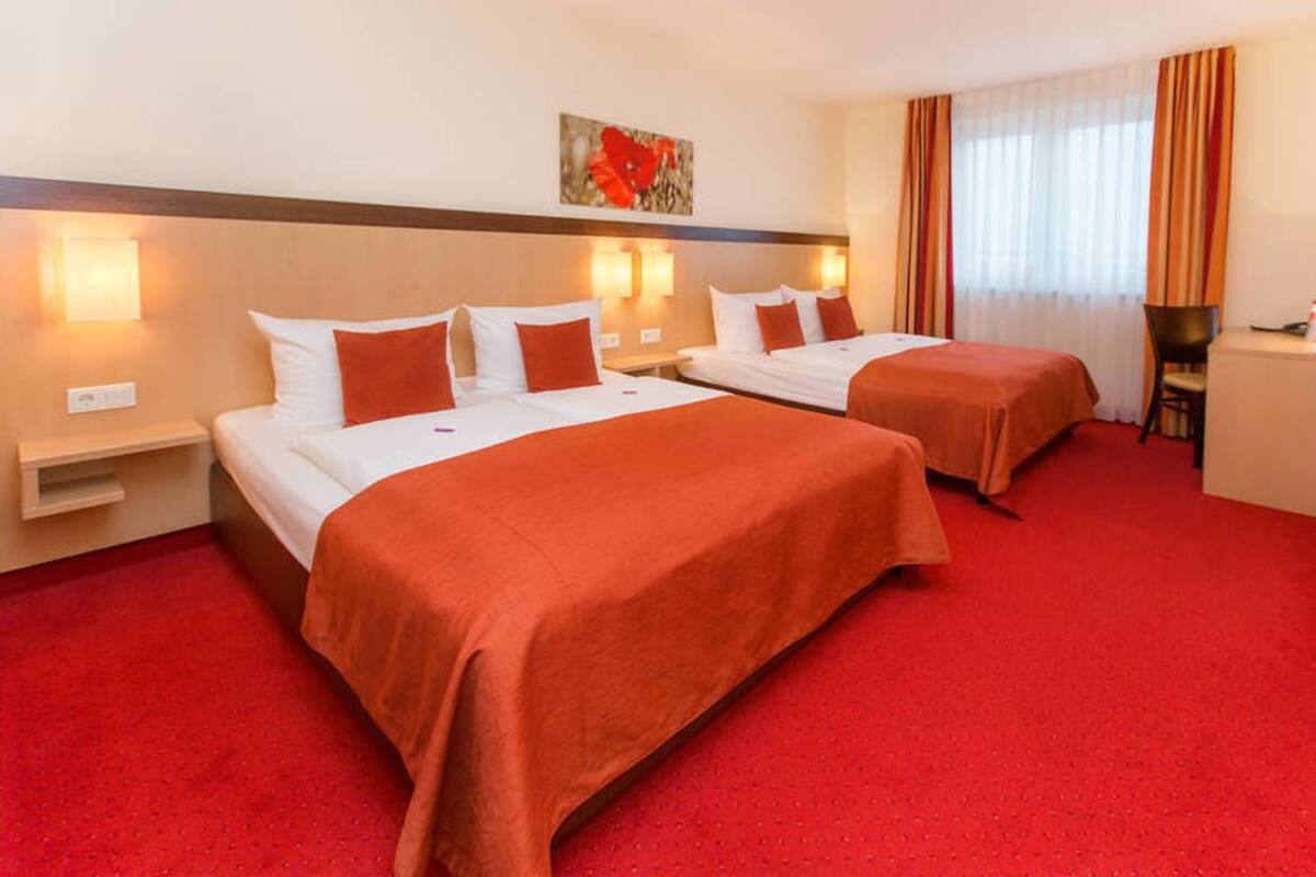 A hotel room with two beds, red carpeting, and a desk with a chair.