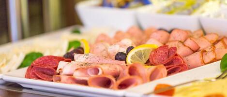 Una bandeja con diversos embutidos y quesos, como salami, jamón y quizás prosciutto, decorada con rodajas de limón y aceitunas.