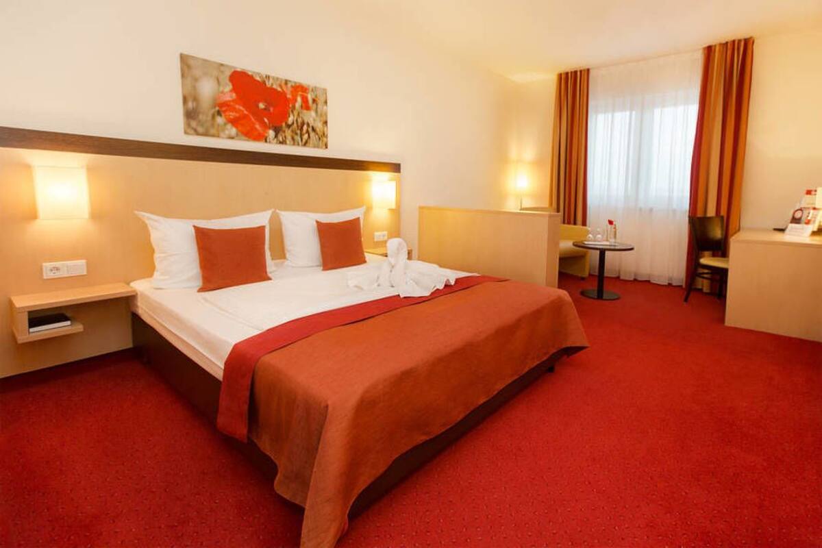 A hotel room with a large bed, a desk, a chair, and a small table.
