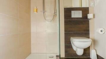 Un baño moderno con cabina de ducha de vidrio, inodoro blanco y suelo de baldosas marrón oscuro.