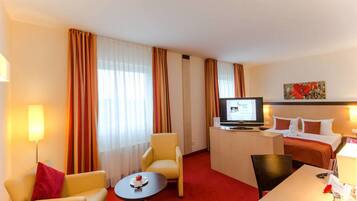 Habitación de hotel con cama, escritorio, computadora, silla, una mesita y televisor.