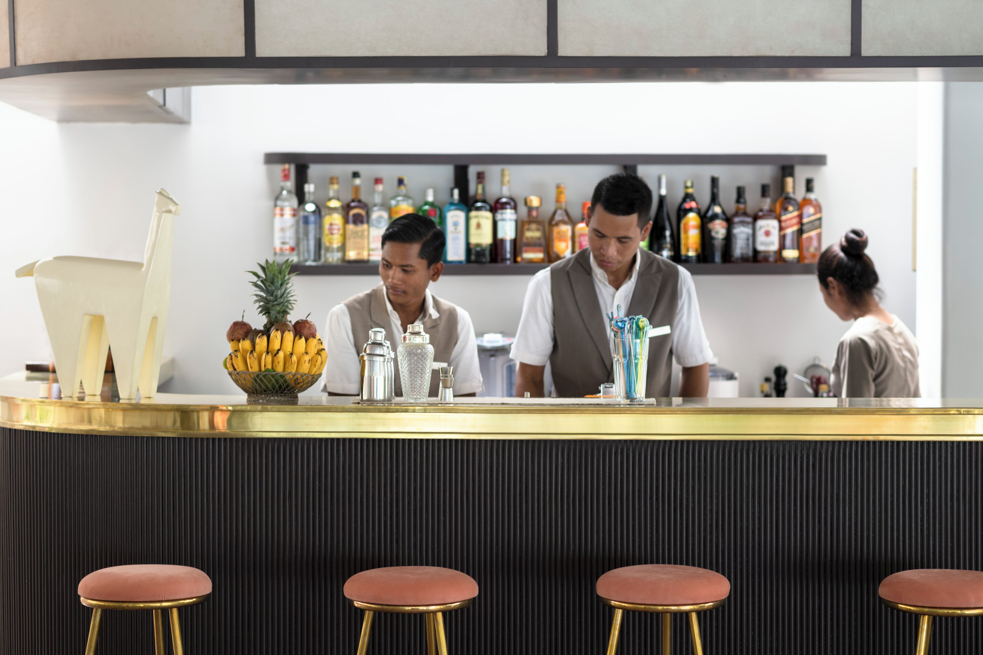 Un espace bar avec un comptoir, des tabourets et une étagère où sont exposées différentes bouteilles.