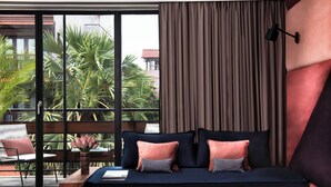 Quarto moderno com grande janela, sofá-cama, mesa de cabeceira com um vaso e vista para palmeiras.