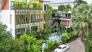 Um edifício moderno com um jardim no terraço, uma piscina e um carro antigo estacionado em frente.