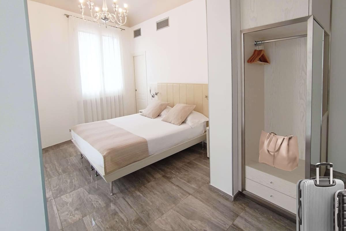 Ein modernes Schlafzimmer mit großem Bett, einer Kronleuchter, einem begehbaren Kleiderschrank und einem Badezimmer mit Dusche und einem aufgehängten Handtuch.