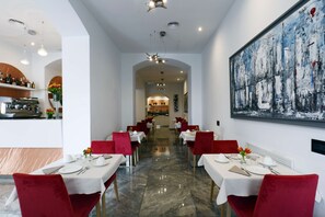 Un restaurant doté d’un sol en marbre, de chaises rouges, de tables blanches et d’un grand tableau abstrait accroché au mur.