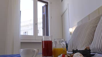 A breakfast tray with a cup, a glass of red juice, a glass of orange juice, and pastries on a table near a window with a view of buildings.