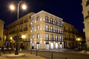 Un immeuble à plusieurs étages, doté de balcons et de fenêtres illuminées la nuit.