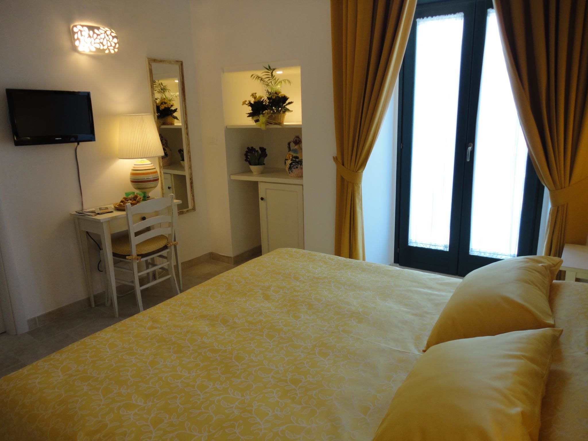 A hotel room with a bed, a desk, a chair, a television, a mirror, and a window with curtains.