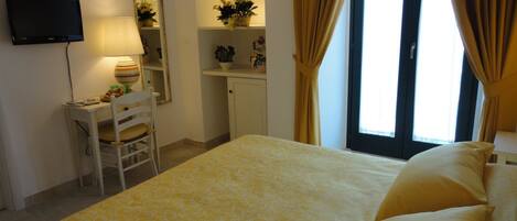 A hotel room with a bed, a desk, a chair, a television, a mirror, and a window with curtains.