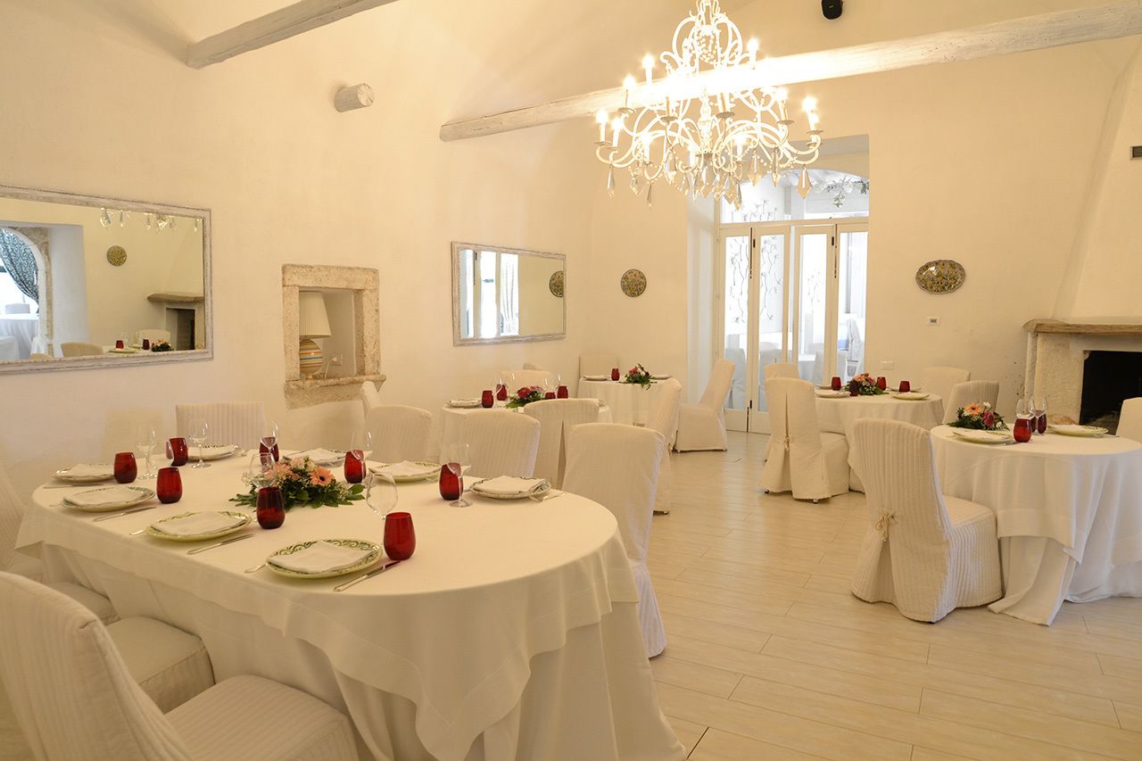 A dining area with round tables set for a meal, white walls, and a chandelier.