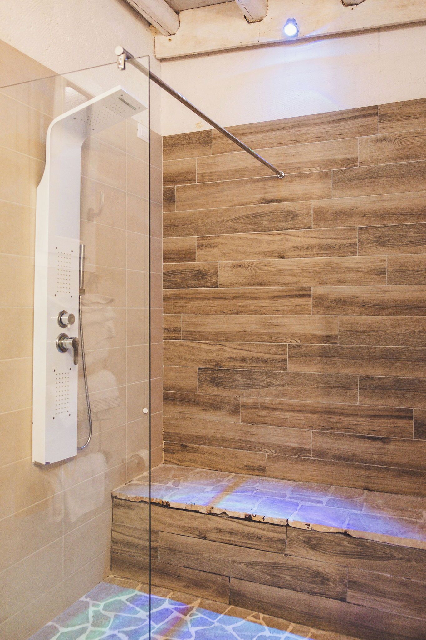 A shower with a glass door, wooden wall tiles, and a bench.