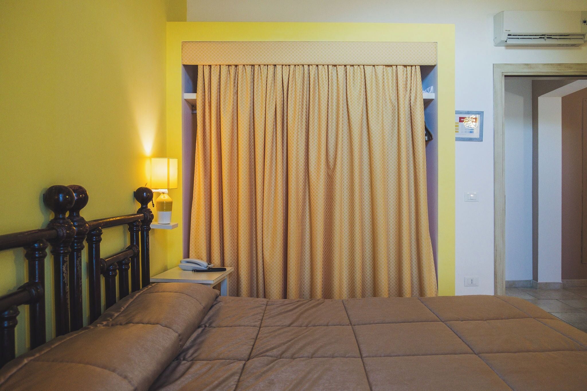 Una habitación de hotel con una cama, una mesita de noche, una lámpara y una cortina.