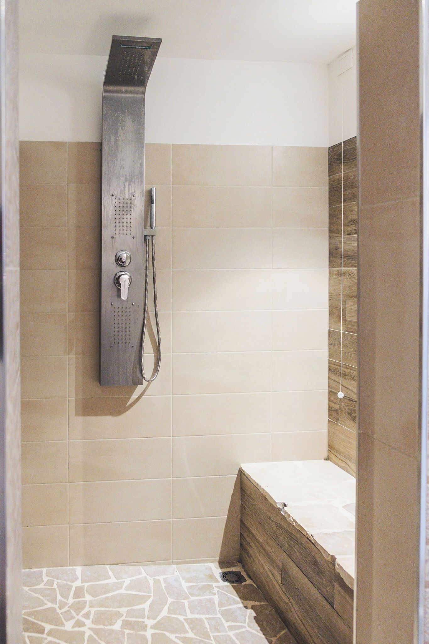 A shower with a handheld showerhead and a wall-mounted control panel.
