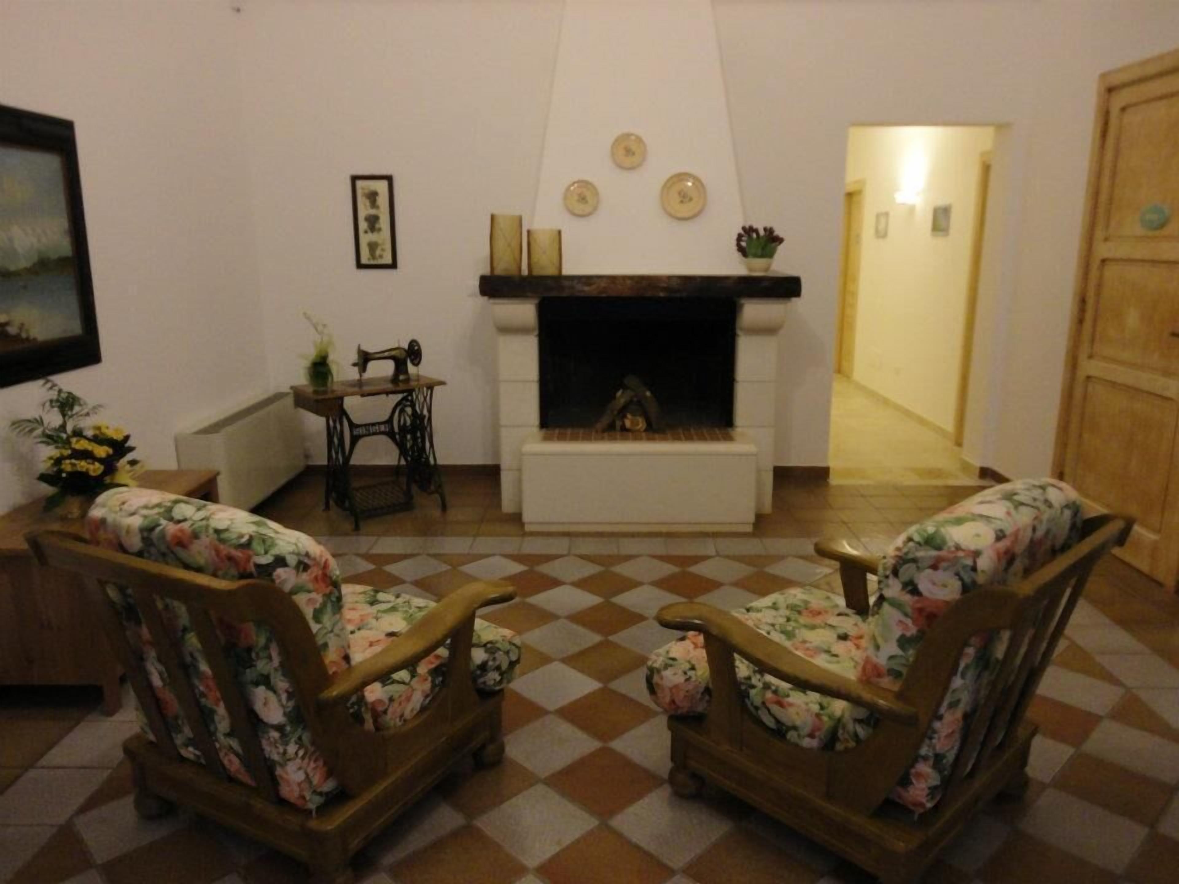Un salon avec deux fauteuils en bois à motifs floraux, une machine à coudre ancienne, une cheminée et un sol à carreaux.