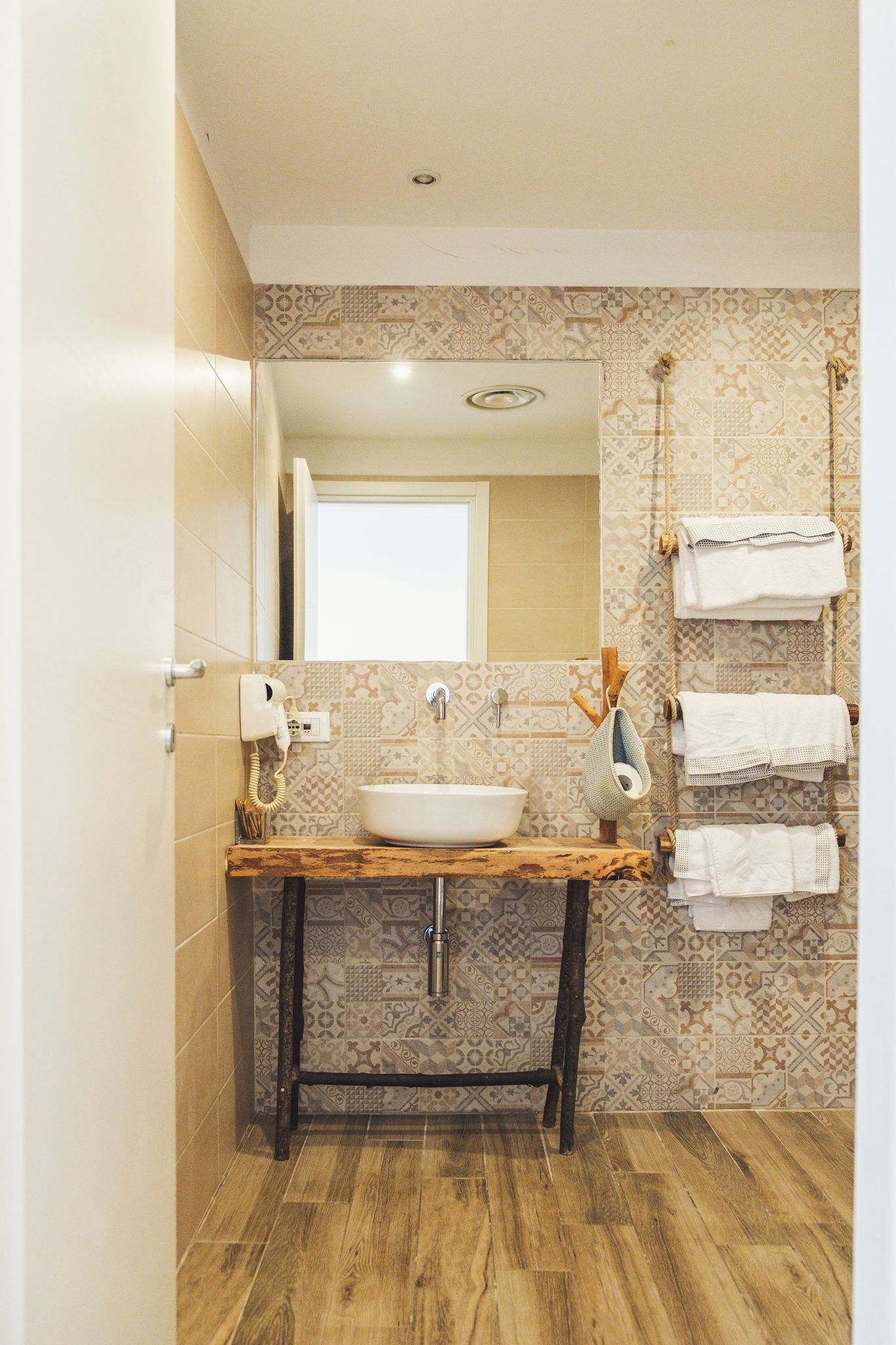 Une salle de bain avec un meuble-lavabo en bois, un lavabo blanc, un miroir et des carreaux décoratifs sur les murs.