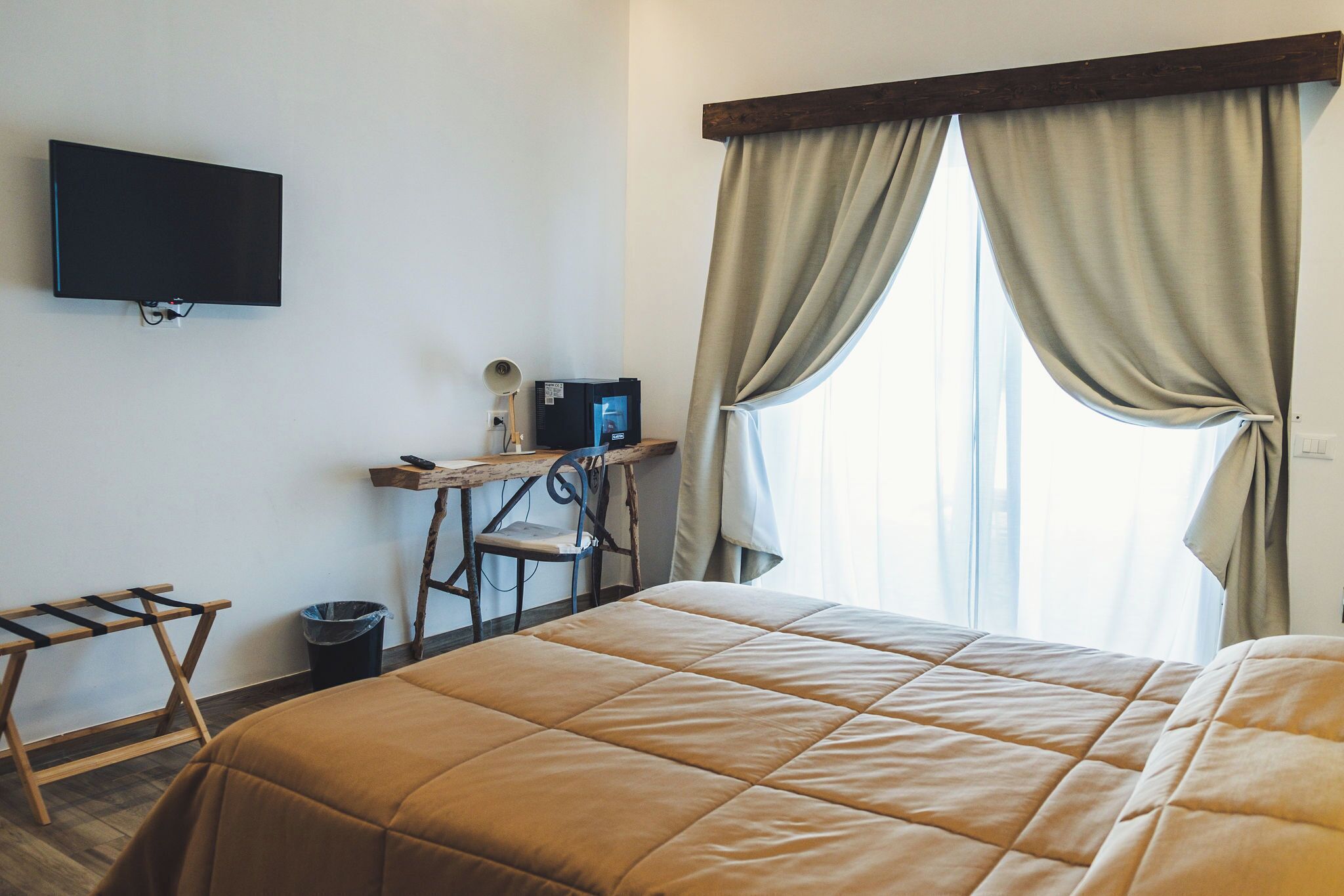 Habitación de hotel con cama, escritorio con computadora, televisor montado en la pared y ventana con cortinas.