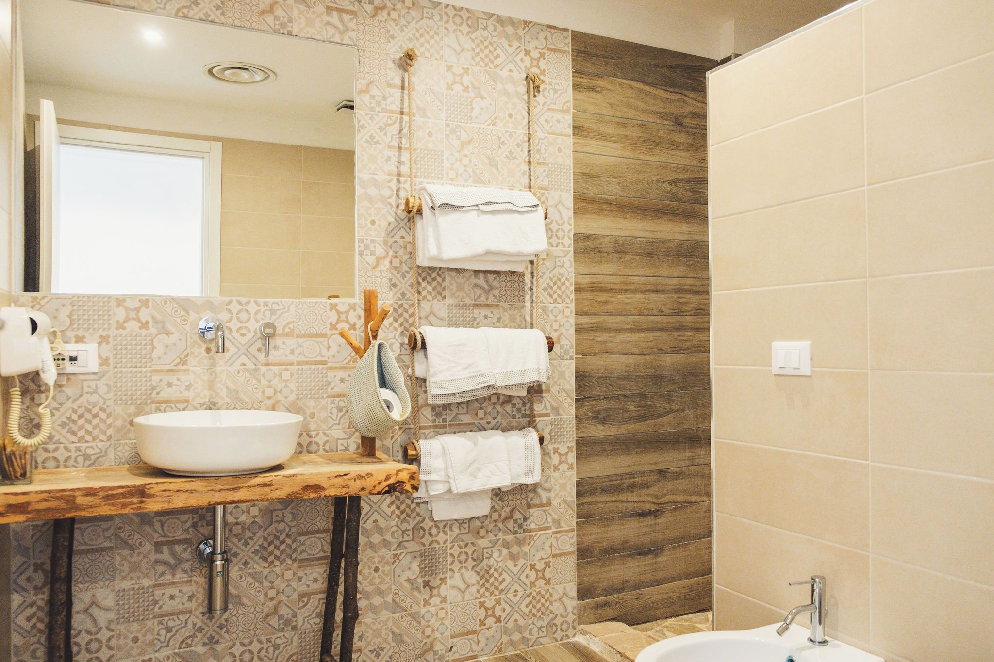 Un baño con tocador de madera, un espejo grande, baldosas estampadas y zona de ducha.