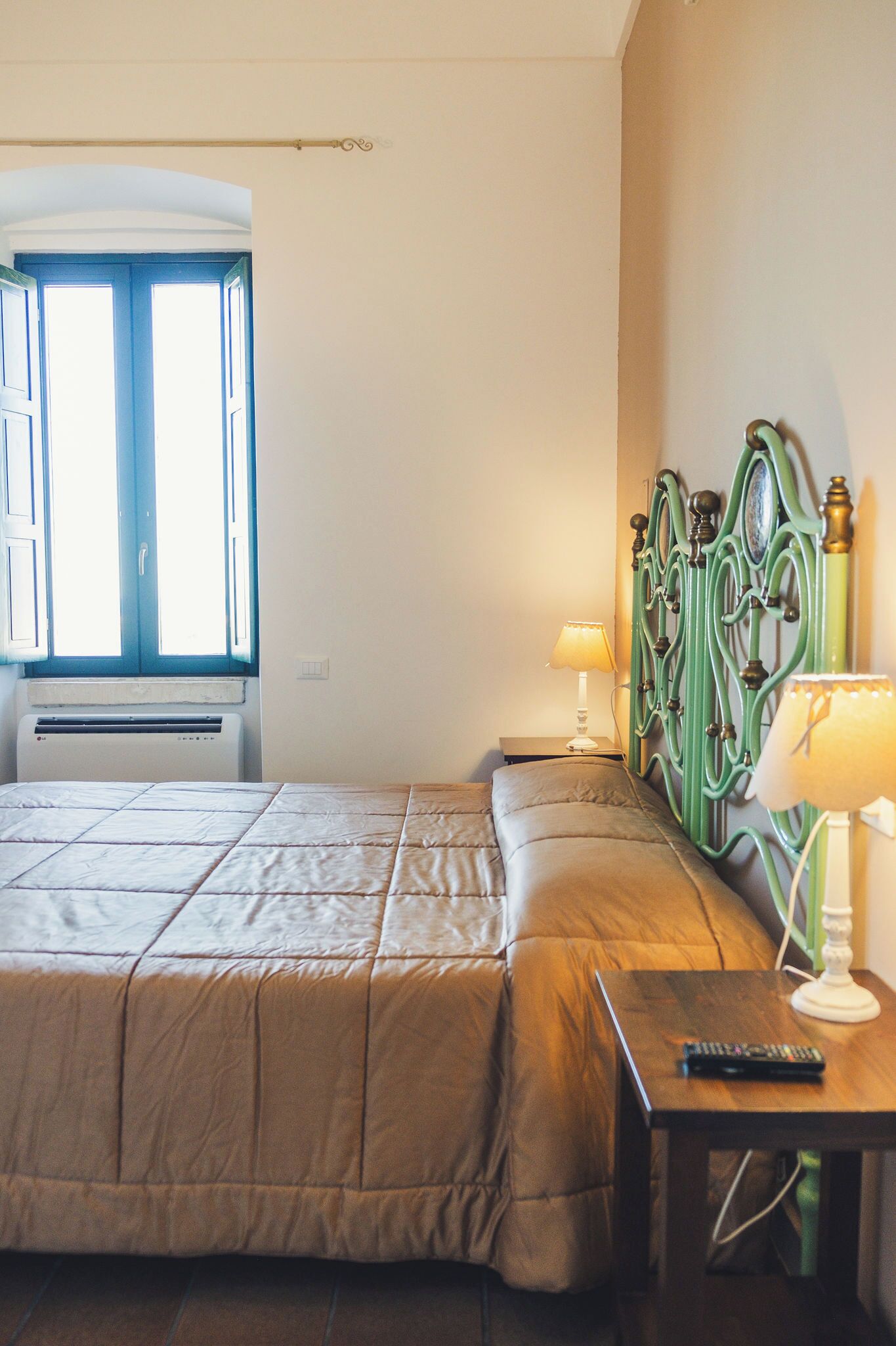 Une chambre à coucher avec un lit, une table de chevet avec une lampe, une fenêtre avec des rideaux et un radiateur.