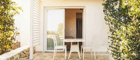 A patio with a table and two chairs, a stone wall, and a door leading to an interior space.