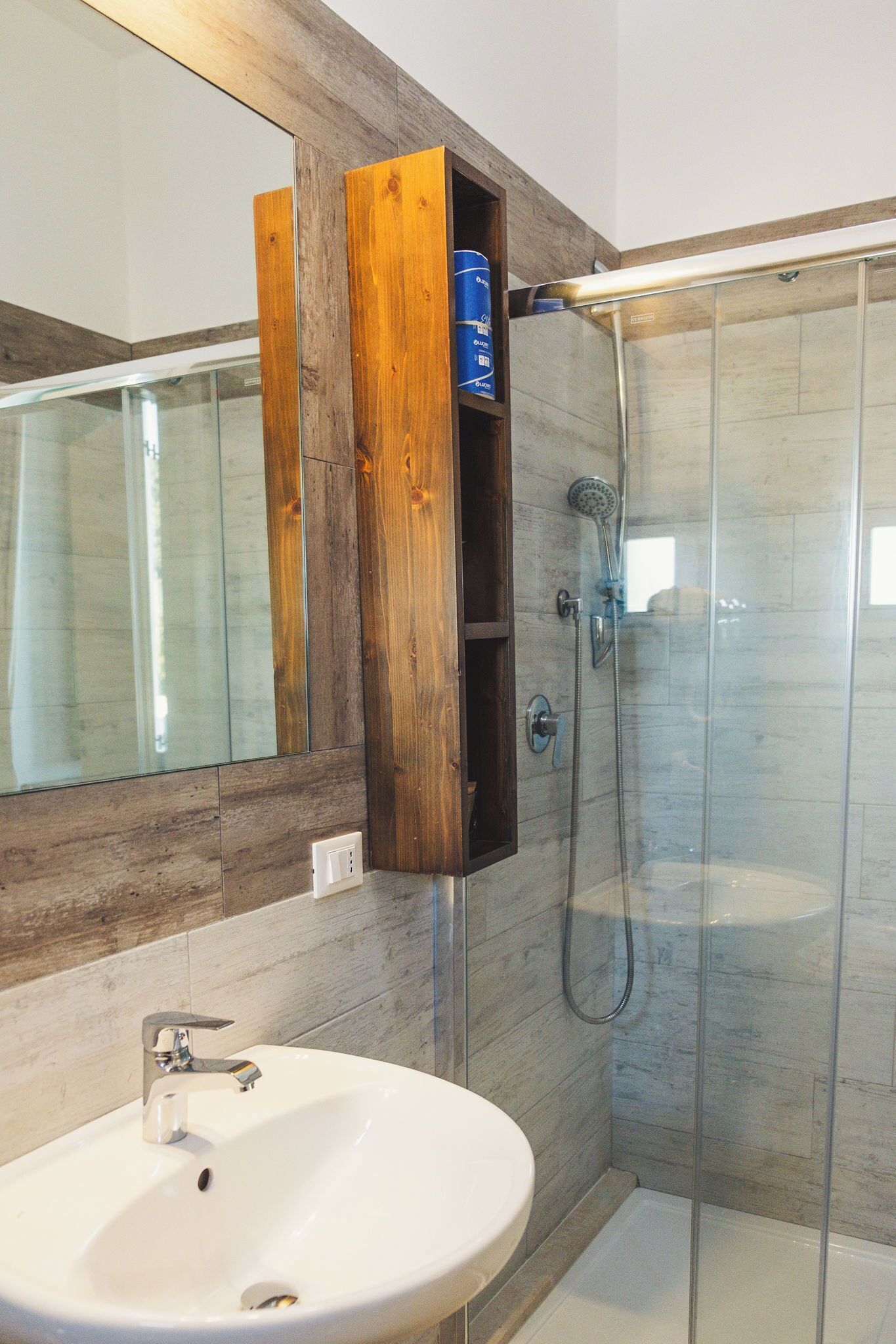 A bathroom with a wooden vanity, a white sink, a glass shower enclosure, and a large mirror.