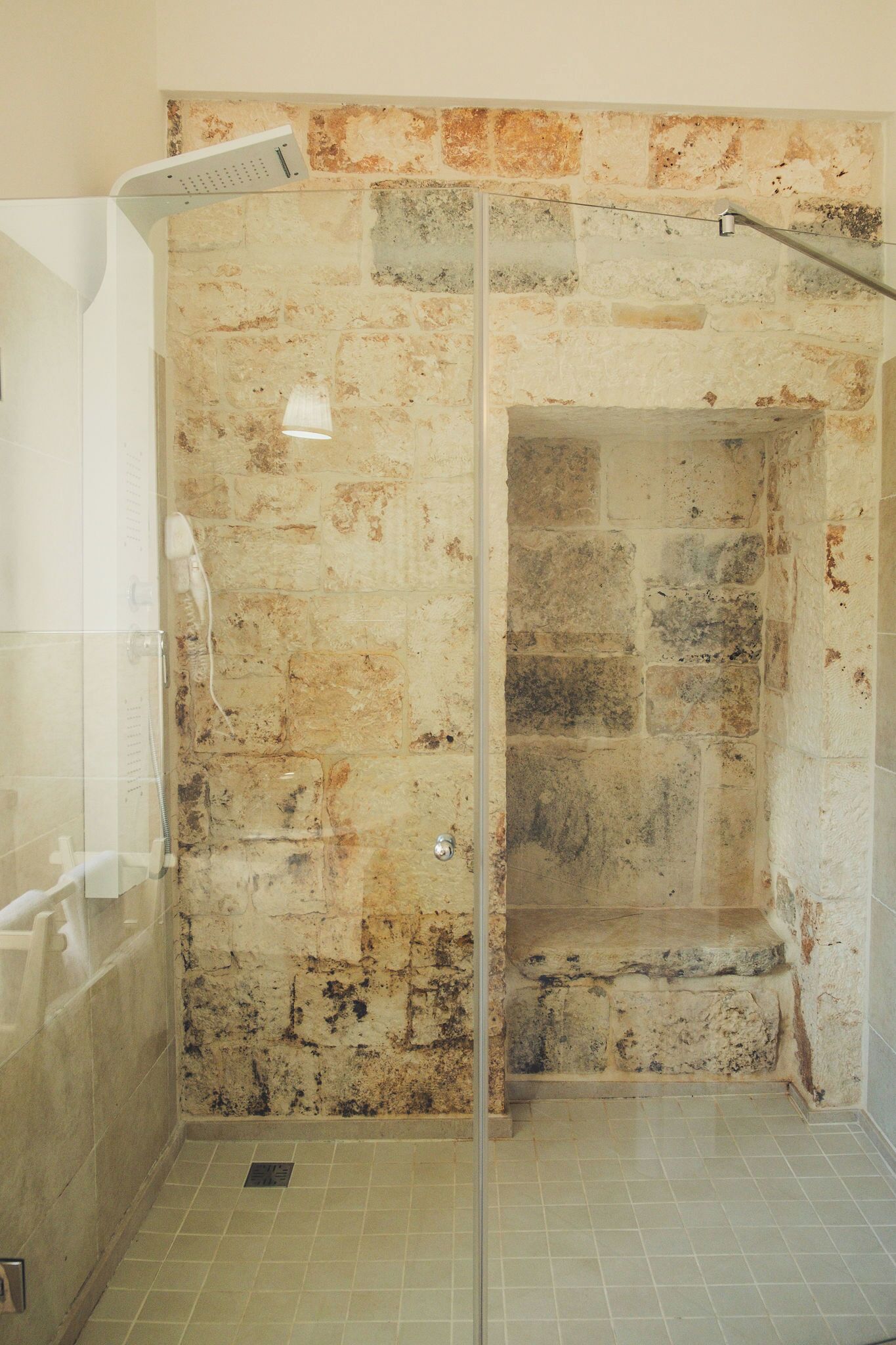Ducha con puerta de vidrio, pared de piedra y suelo de baldosas.