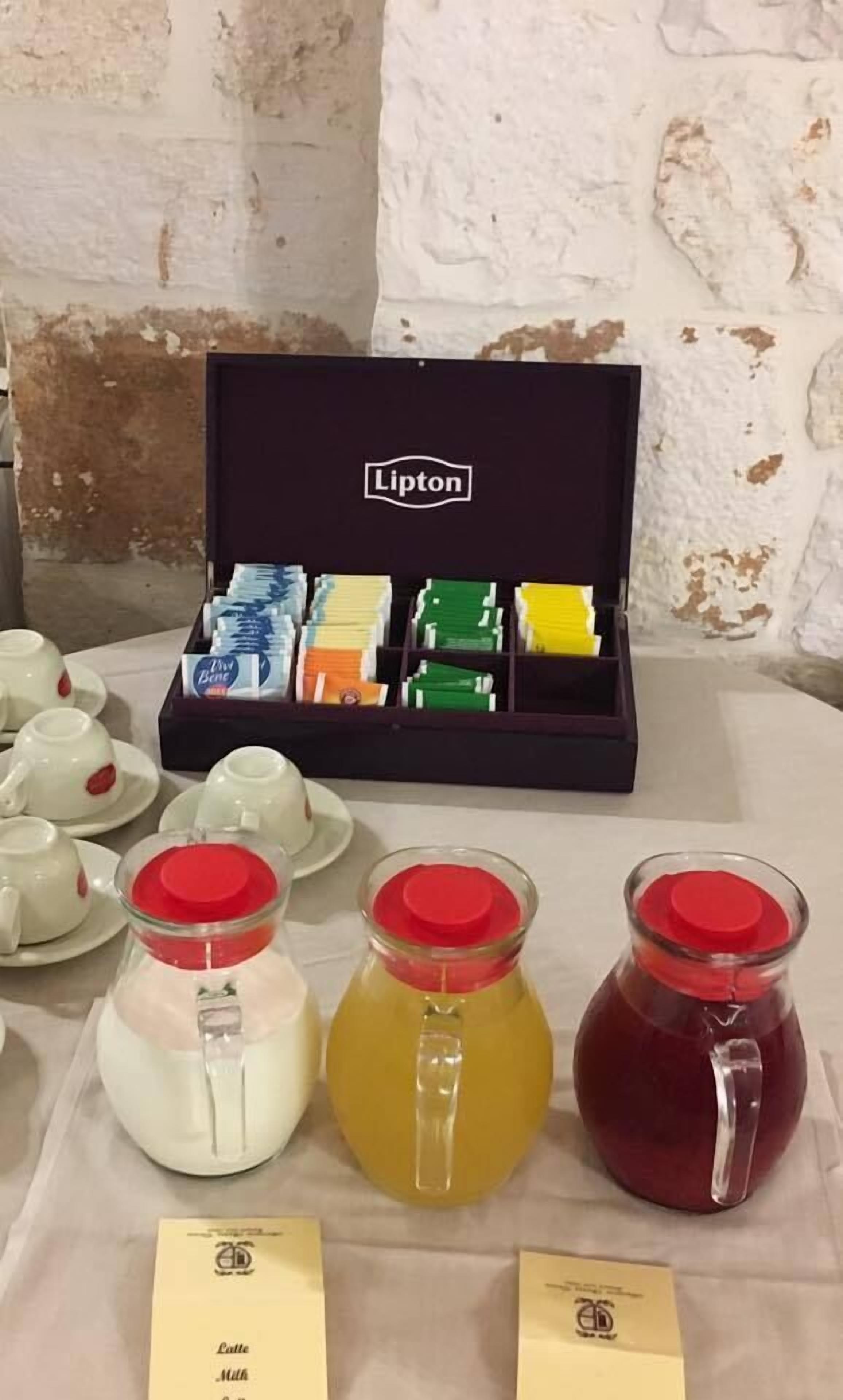 A table with a Lipton tea box, teacups, and three glass containers with different colored liquids.