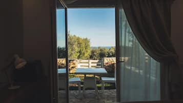 Una habitación con puerta corredera de vidrio que da a un patio exterior con una mesa, sillas, una lámpara y un muro de piedra.