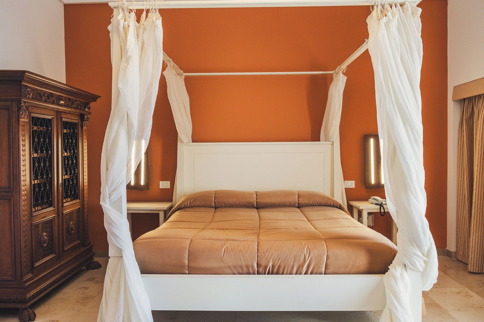 A bedroom with a four-poster bed, a wooden cabinet, and two bedside tables.