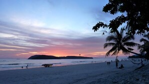 Una playa con un atardecer, palmeras y una isla distante.