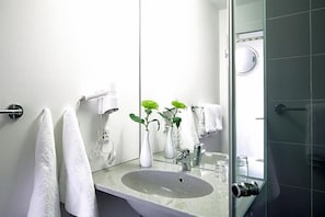 Un baño con lavamanos, espejo y dos jarrones con plantas.