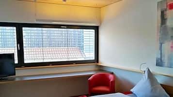 Ein Hotelzimmer mit Bett, einem roten Sessel, einem Fernseher und einem Fenster mit Stadtblick.