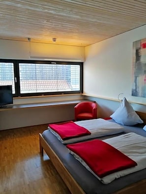 Una habitación de hotel con una cama, una silla roja, un televisor y una ventana con vista a la ciudad.