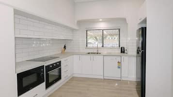 A modern kitchen with white cabinetry, a black refrigerator, and a window with blinds.
