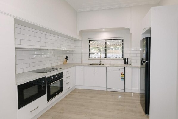 A modern kitchen with white cabinetry, a black refrigerator, and a window with blinds.