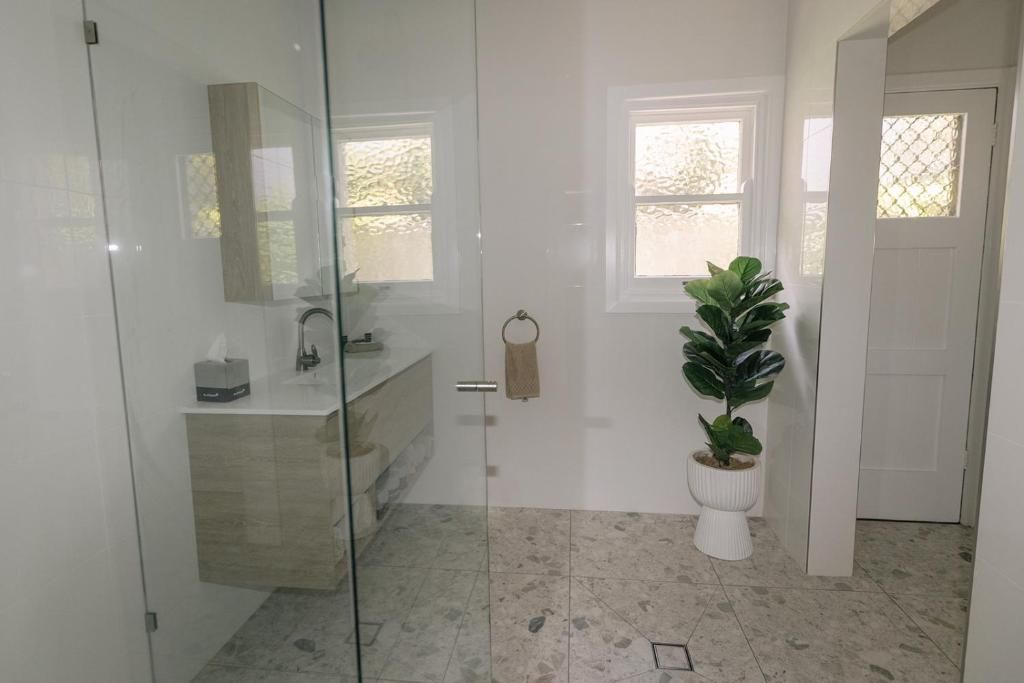 A modern bathroom with a glass shower enclosure, a sink with a mirror, a potted plant, and a door with a towel ring.