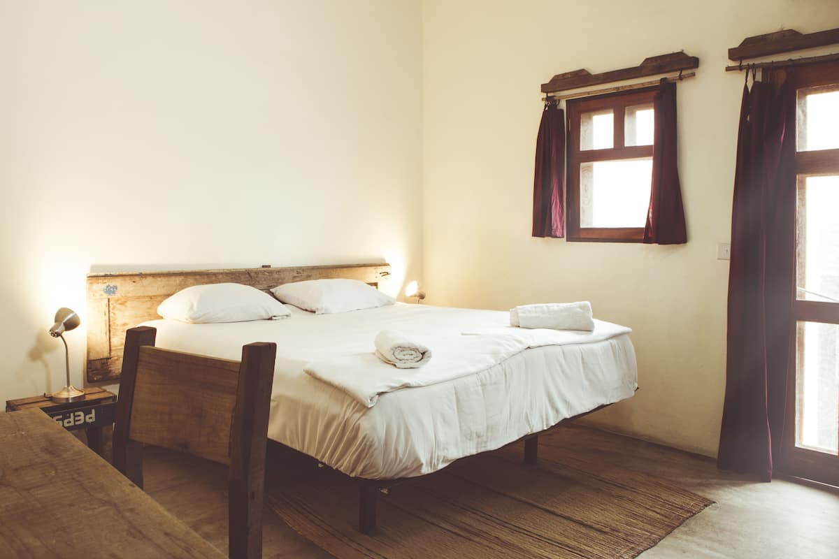 A single bed with white linens, a wooden headboard, and a bedside lamp.